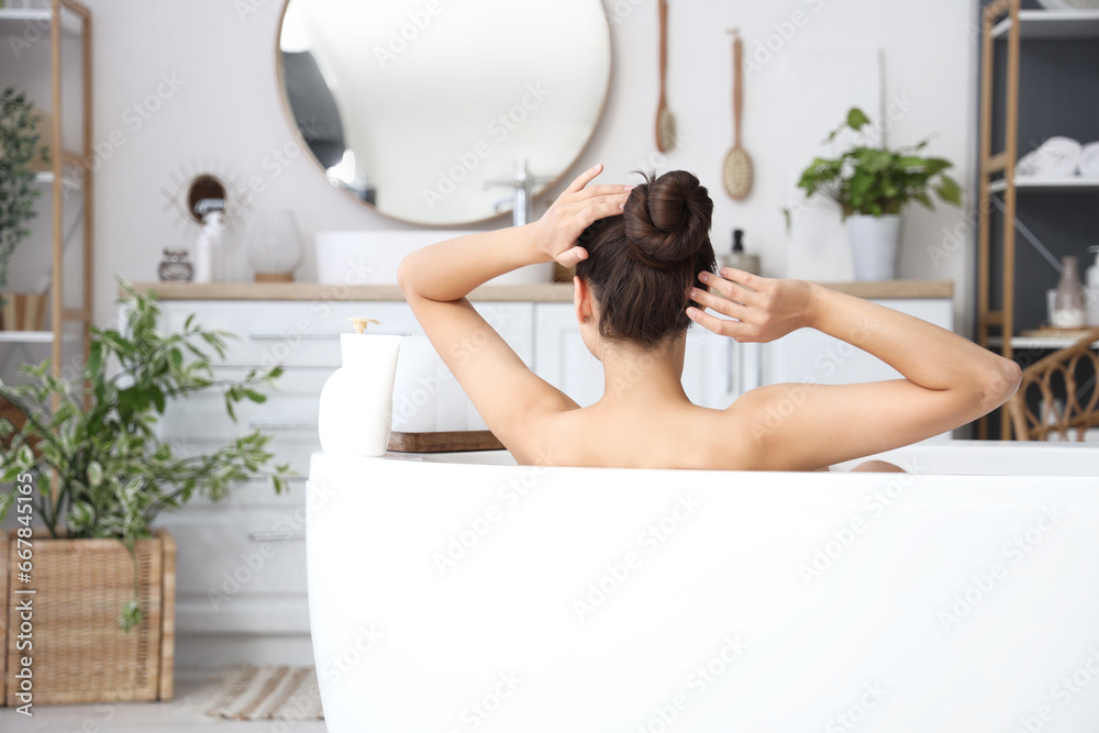 Young woman taking bath at home, back view