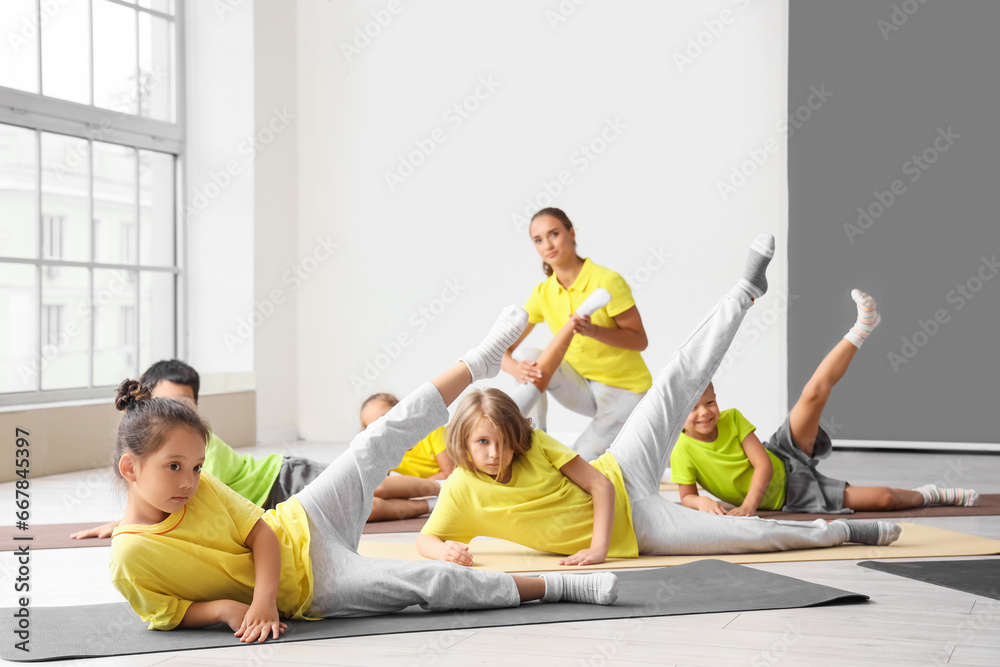 Group of little children with instructor practicing yoga in gym