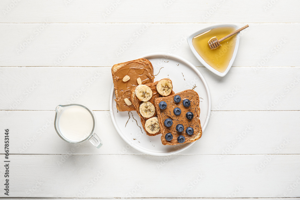 Plate of toasts with peanut butter, fresh fruits and nuts on white wooden background