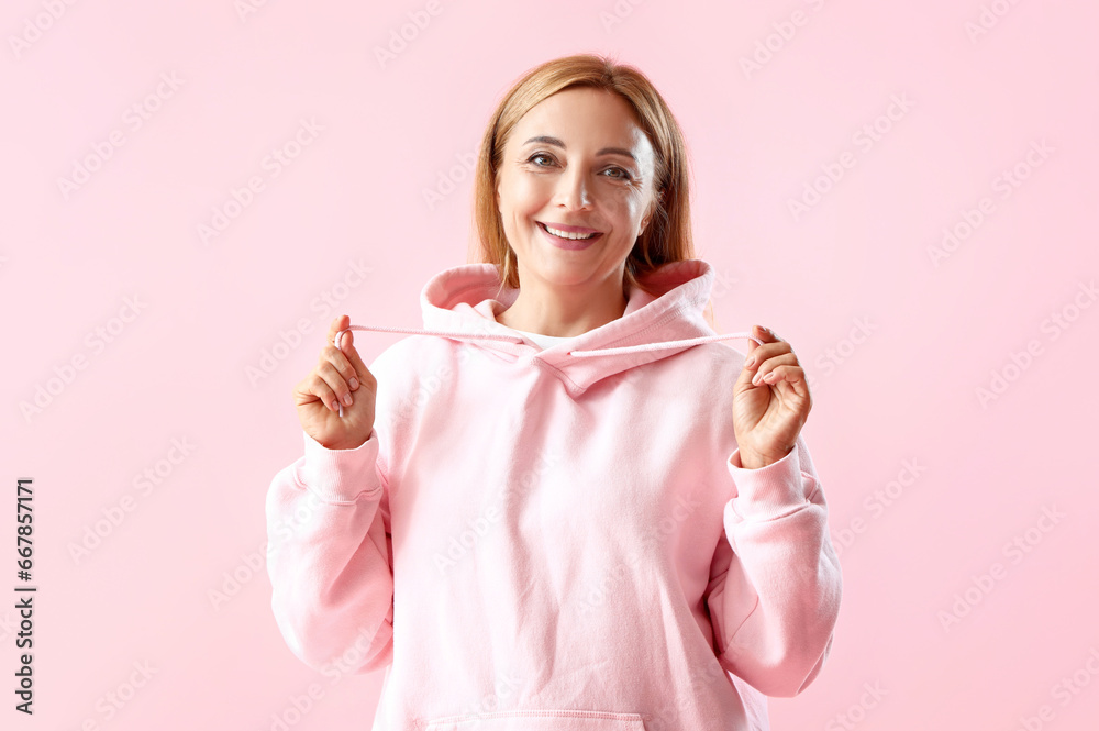 Mature woman in hoodie on pink background