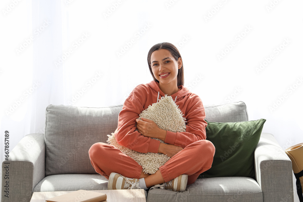 Young woman in hoodie with pillow sitting on sofa at home