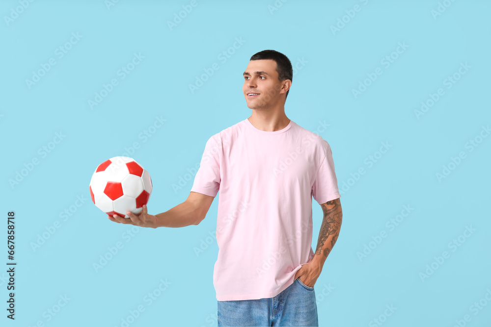 Handsome young man with soccer ball on blue background