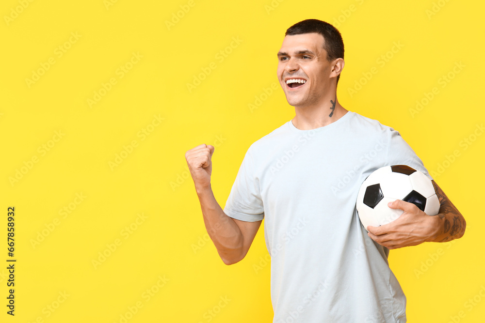 Handsome young man with soccer ball on yellow background