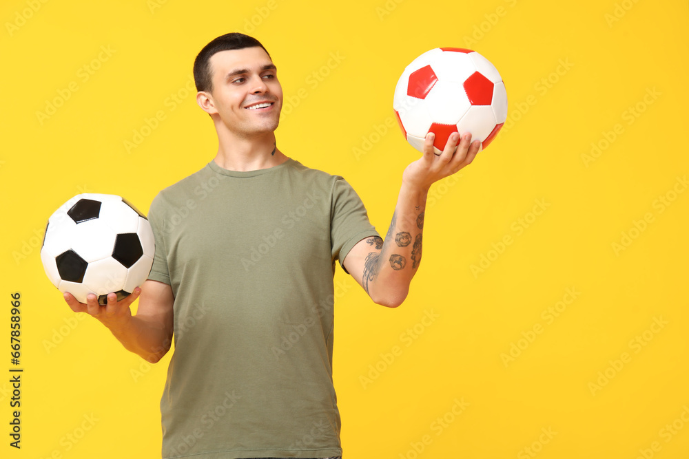 Handsome young man with soccer balls on yellow background