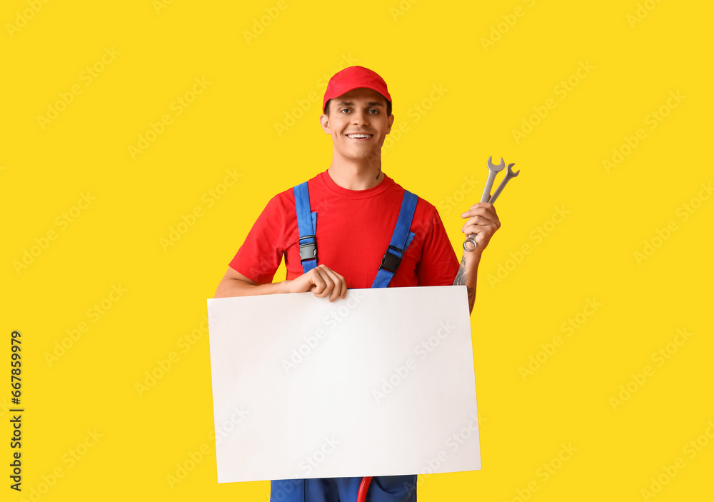 Male car mechanic with wrenches and blank poster on yellow background