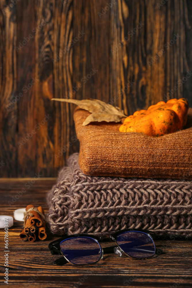 Stack of warm clothes, eyeglasses, pumpkin and cinnamon on wooden background, closeup