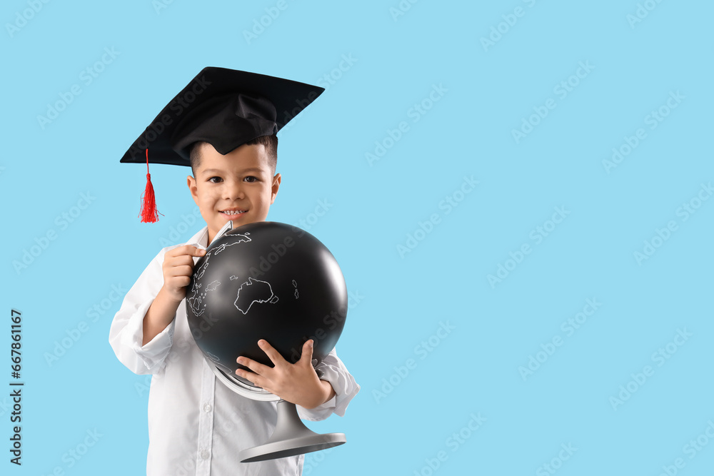 Little Asian boy in graduation hat with globe on blue background