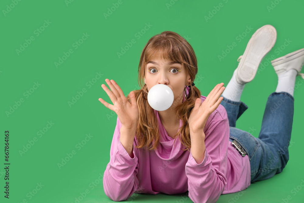 Beautiful young woman with chewing gum lying on green background