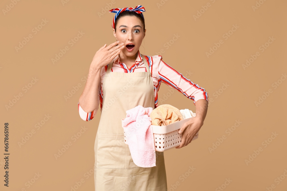 Portrait of shocked young housewife in apron with dirty laundry on brown background