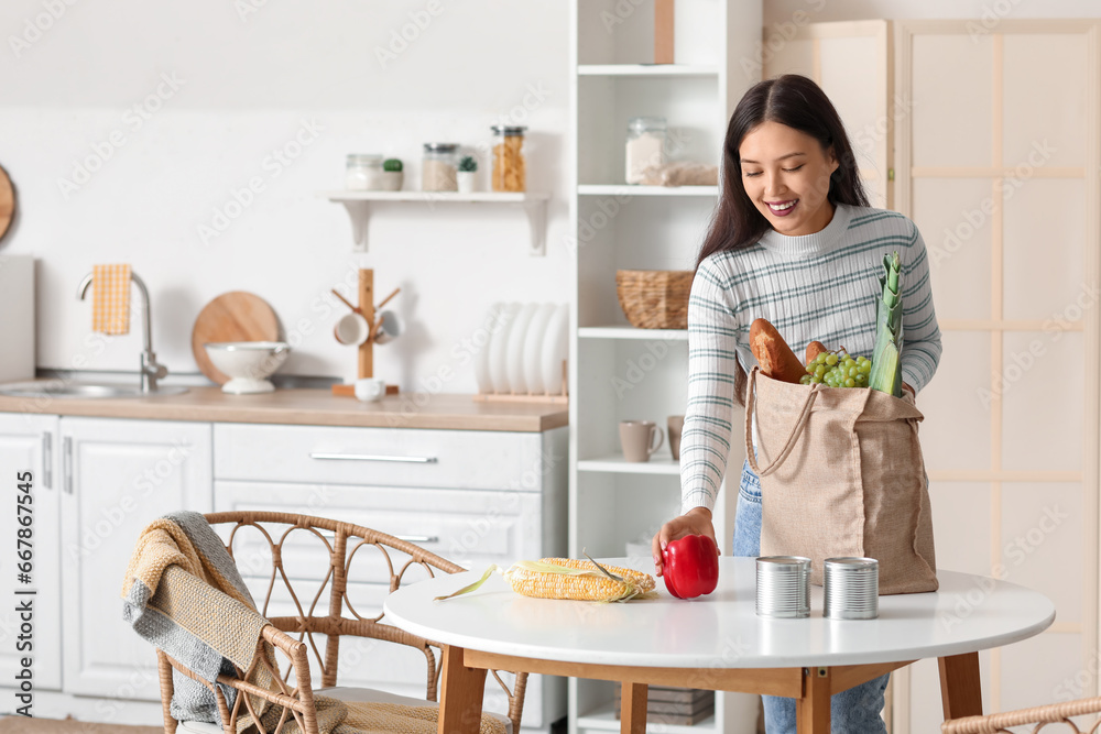 Young Asian woman unpacking fresh products from market at table in kitchen