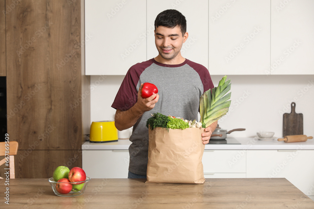 Young man with grocery bag at table in kitchen