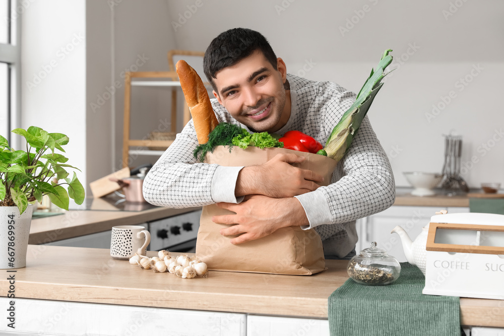 Young man with grocery bag at table in kitchen