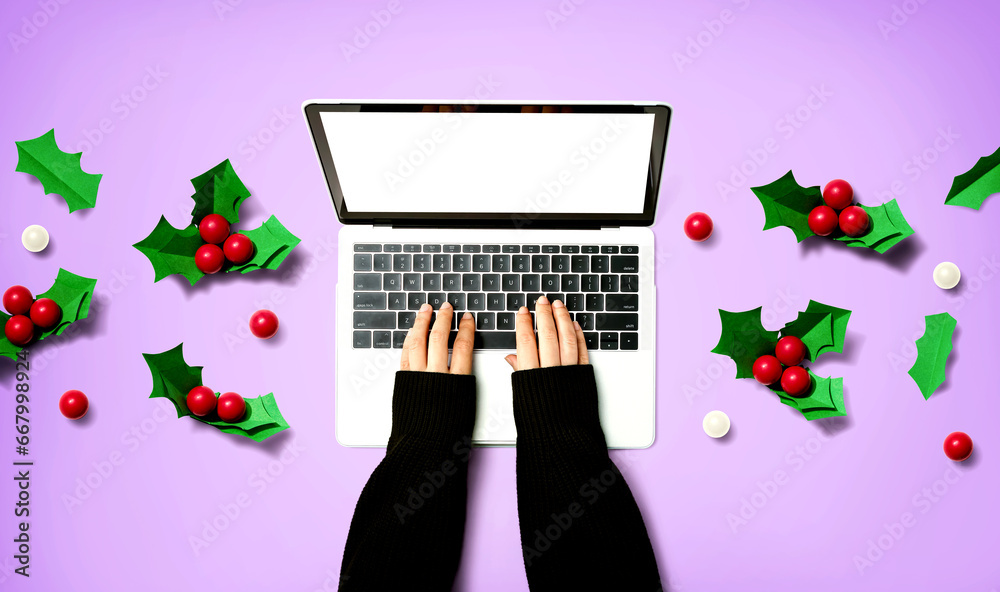 Person using a laptop computer with Christmas holly berries from above