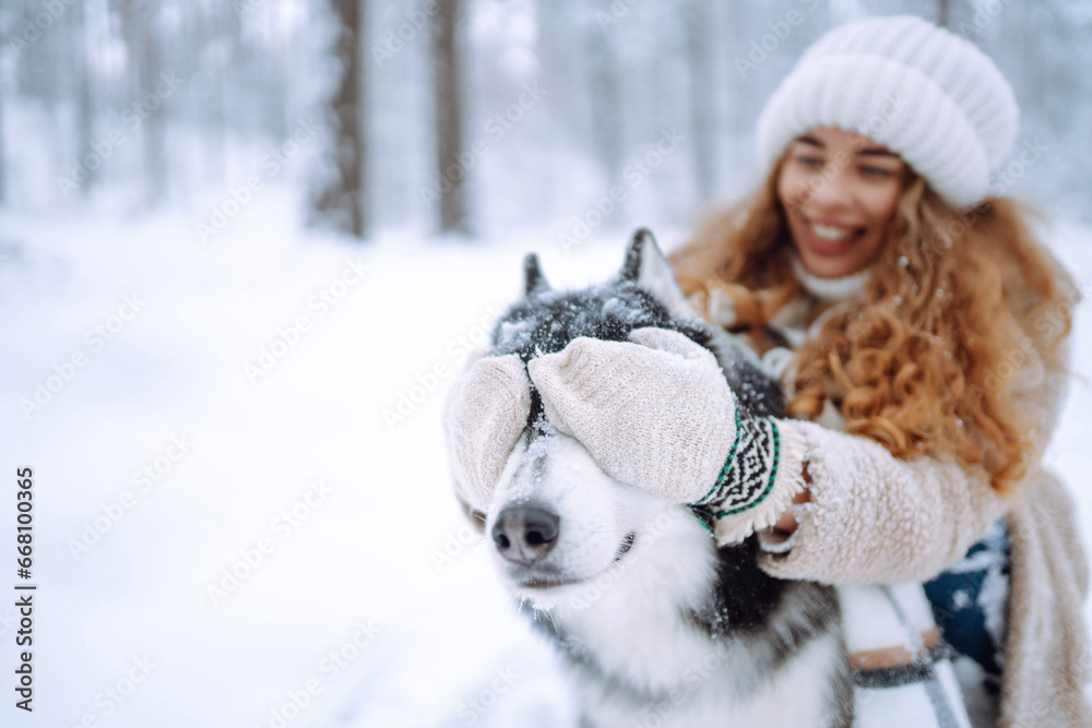 Beautiful young woman plays with her dog in the winter forest. First snow. Friendship, love and devotion concept. Outdoor recreation