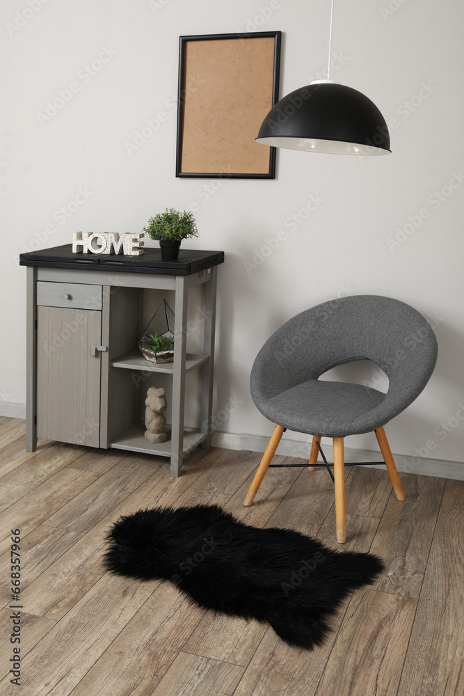 Interior of living room with stylish grey armchair and modern cabinet near white wall