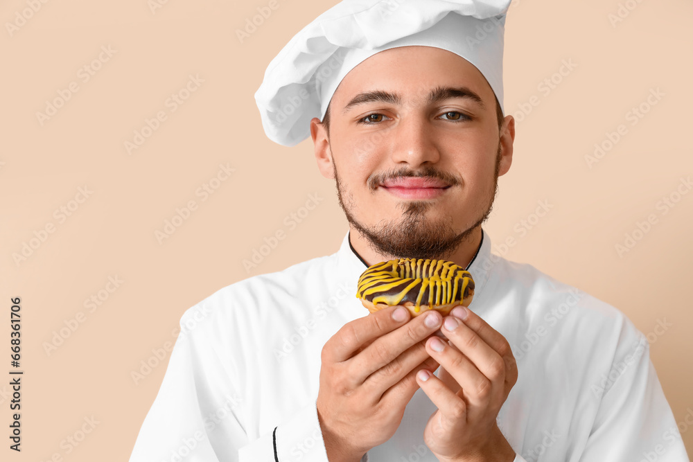 Male chef with tasty doughnut on beige background, closeup