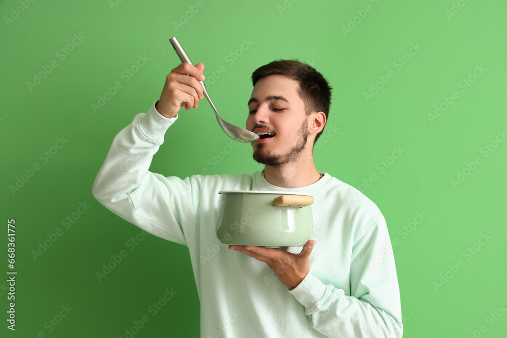 Young man with ladle and cooking pot on green background