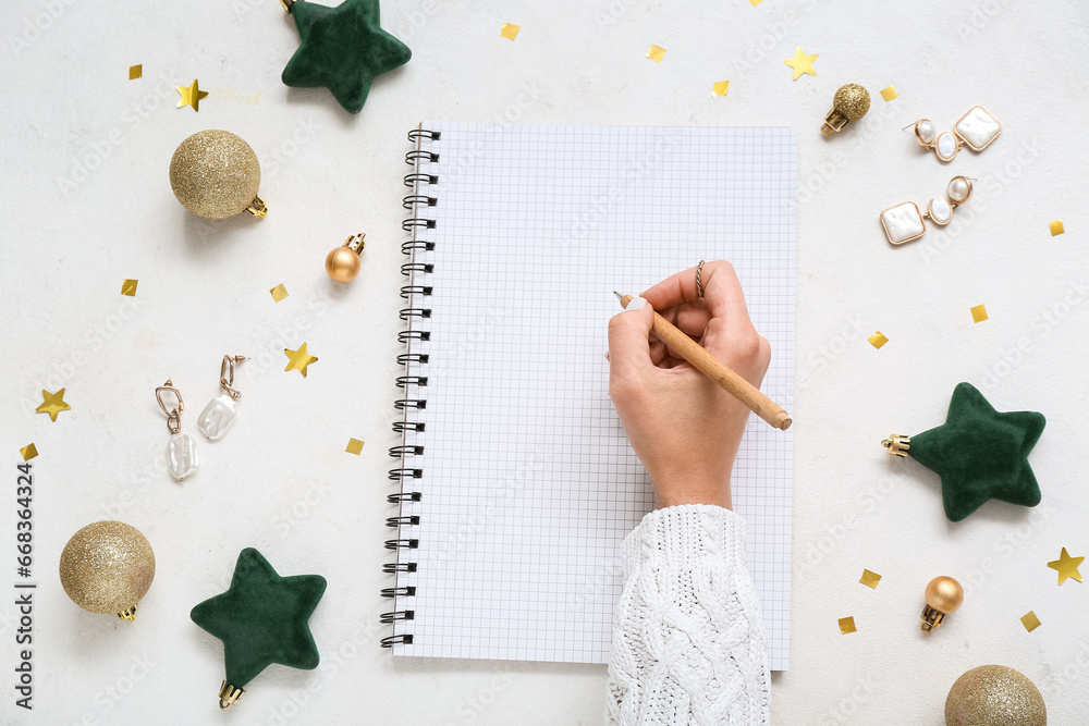 Woman writing in notebook with Christmas decor and earrings on white background