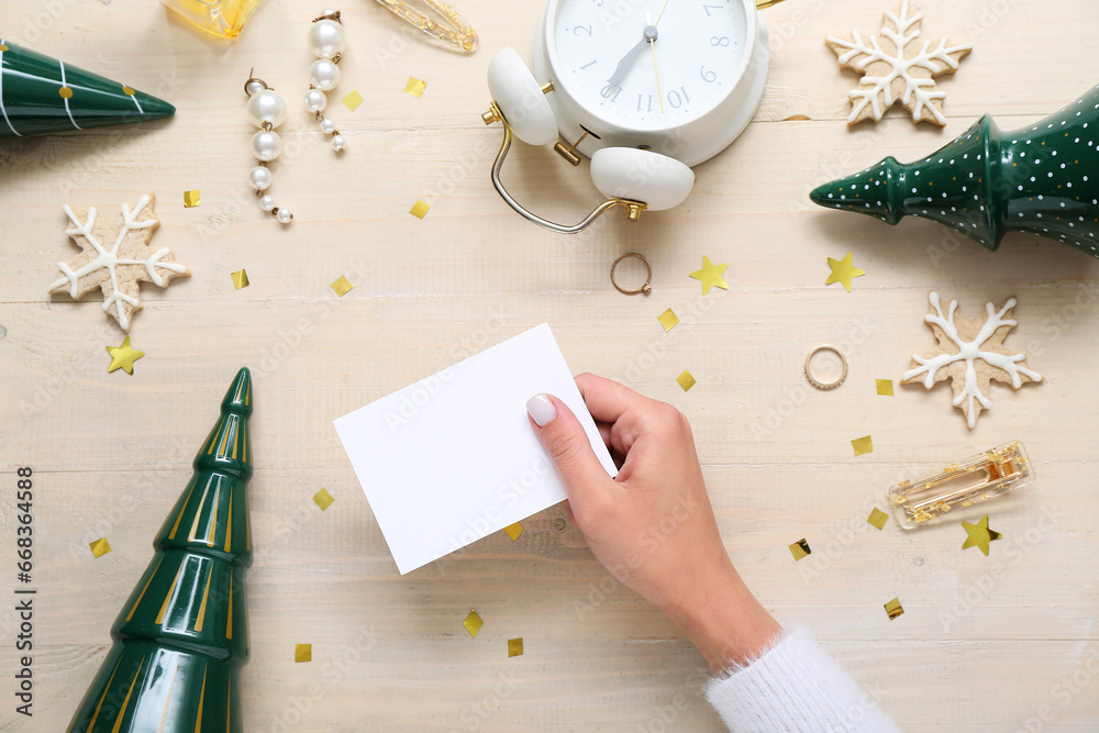 Woman with blank card, cookies, accessories and Christmas decor on light wooden background