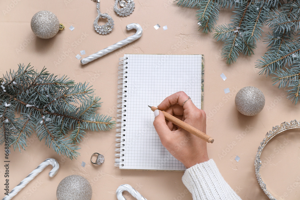 Woman writing in notebook with Christmas decor and accessories on beige background