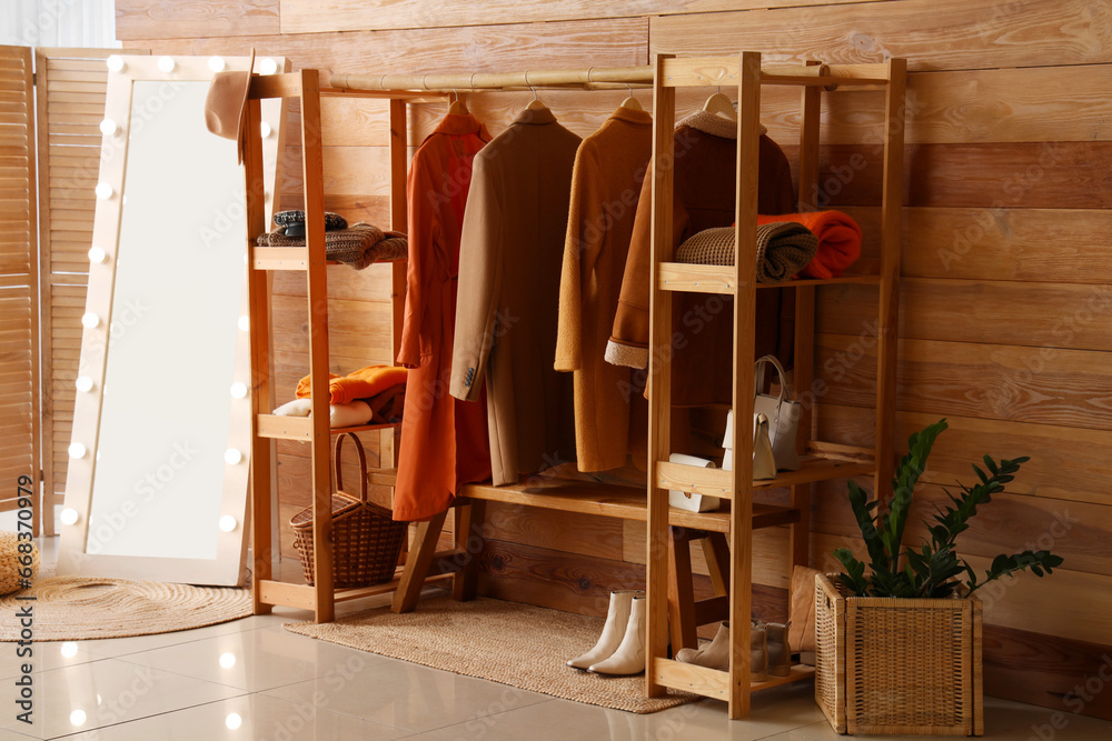 Rack with stylish autumn clothes and mirror in interior of modern hallway