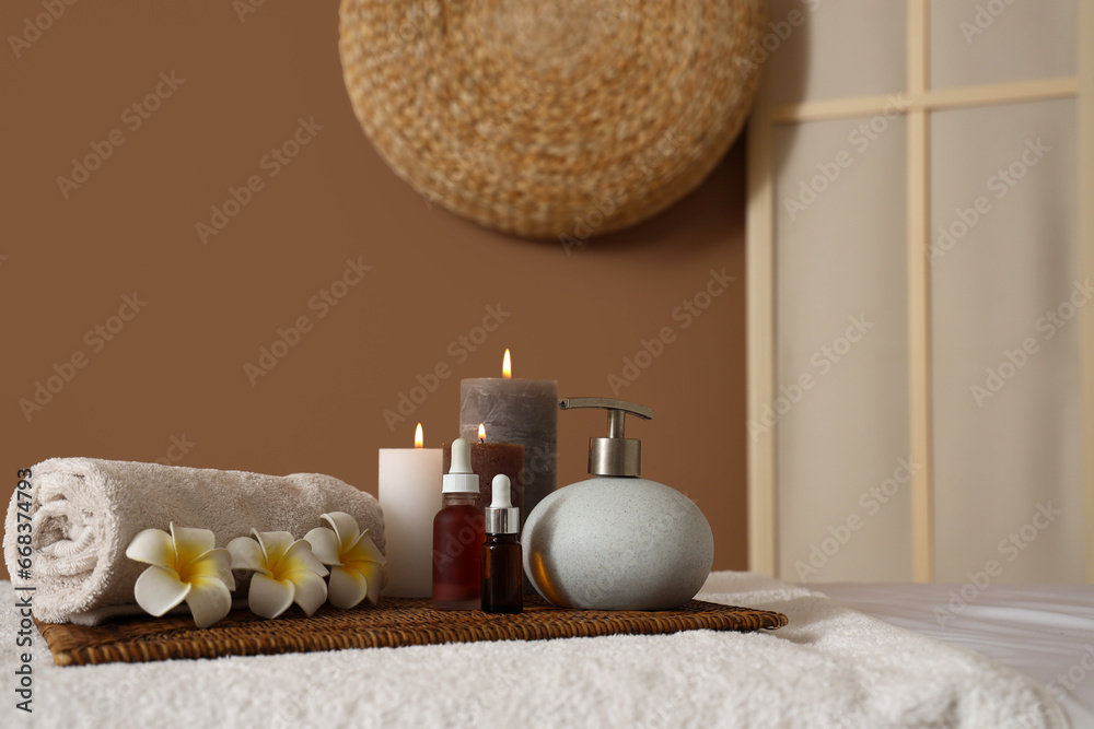 Spa composition with burning candles and flowers on couch in salon, closeup