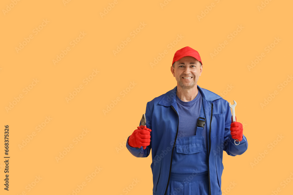 Portrait of male mechanic with tools on orange background