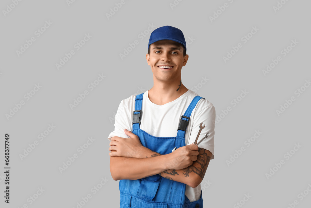 Male car mechanic with crossed arms and wrenches on grey background