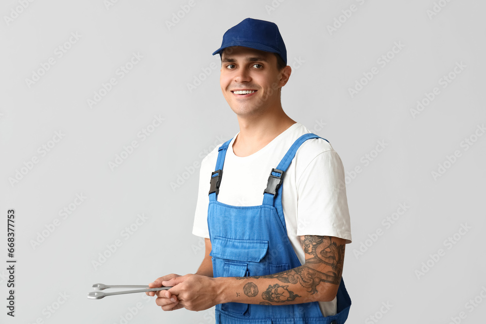 Male car mechanic with wrenches on grey background