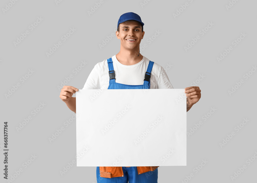 Male car mechanic with blank poster on grey background