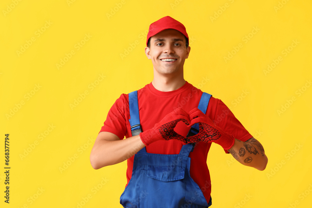 Male car mechanic showing heart gesture on yellow background