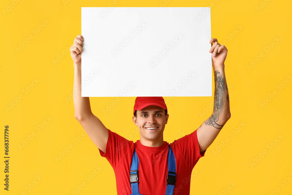 Male car mechanic with blank poster on yellow background