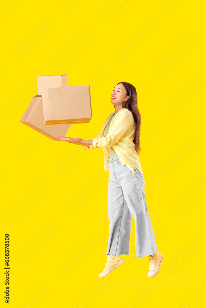 Young Asian woman with parcels jumping on yellow background