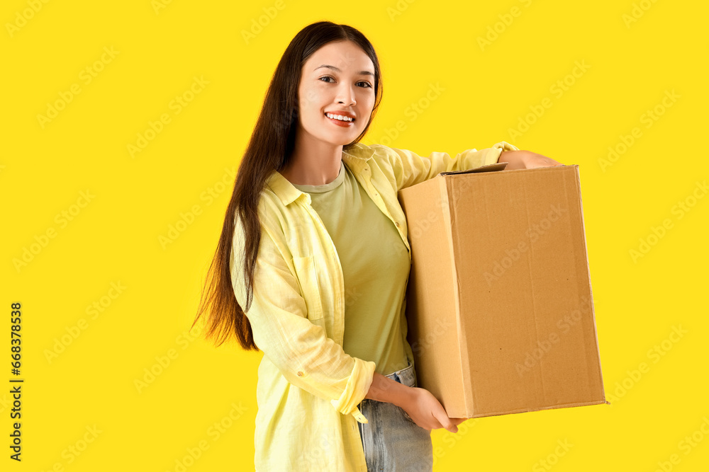 Young Asian woman with parcel on yellow background