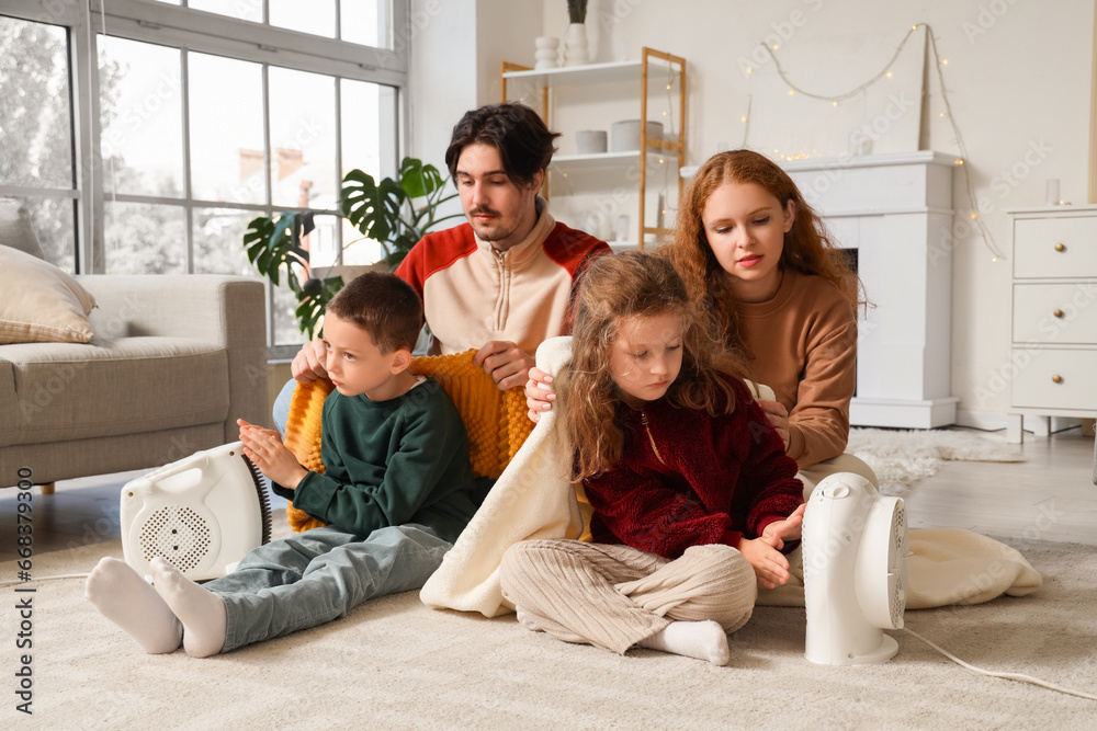 Frozen family warming near electric fan heaters at home with lack of heating