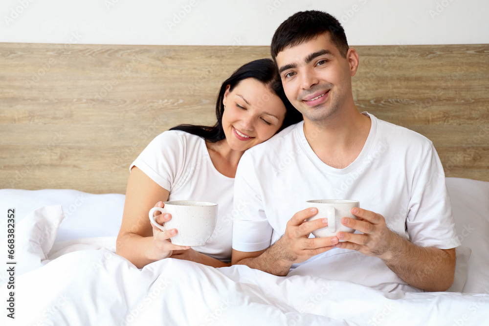 Young couple with cups of coffee in bedroom