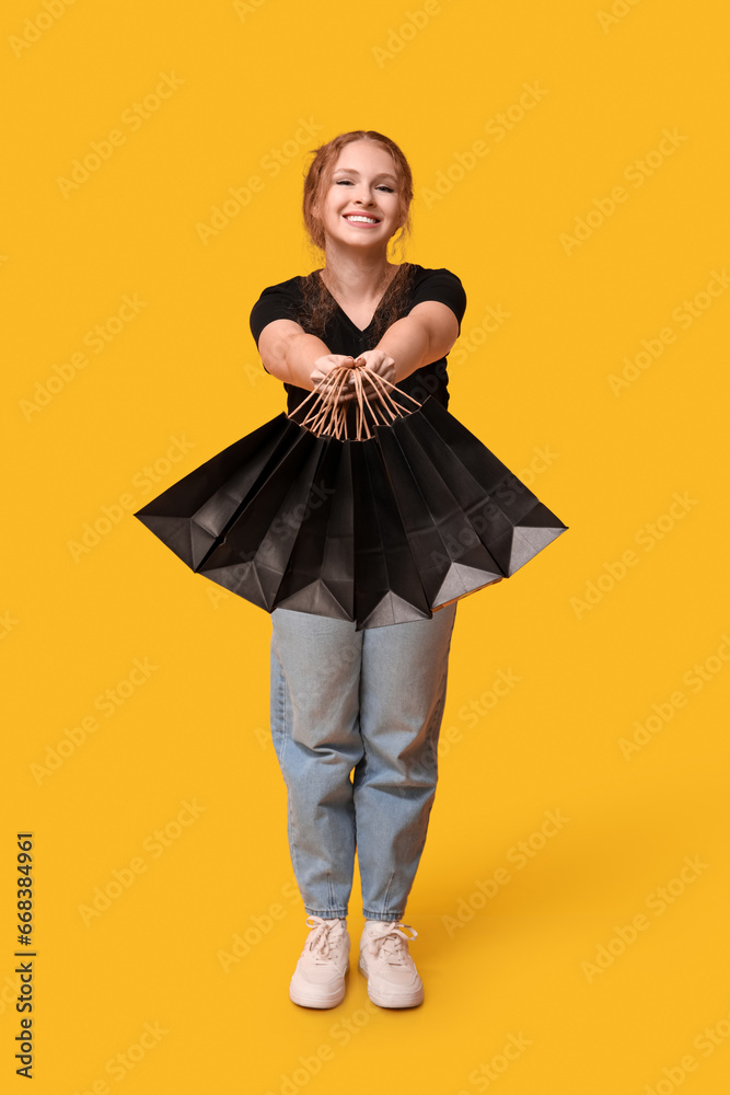 Beautiful young woman with shopping bags on yellow background. Black Friday sale