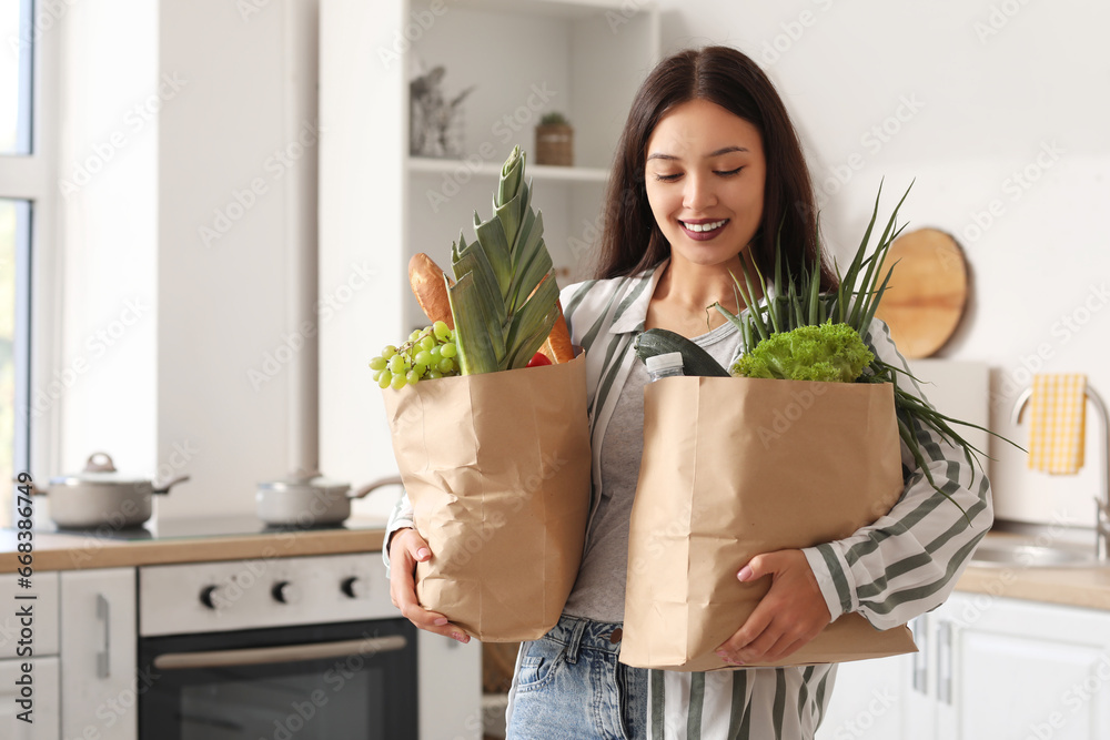 Young Asian woman with shopping bags full of fresh food in kitchen