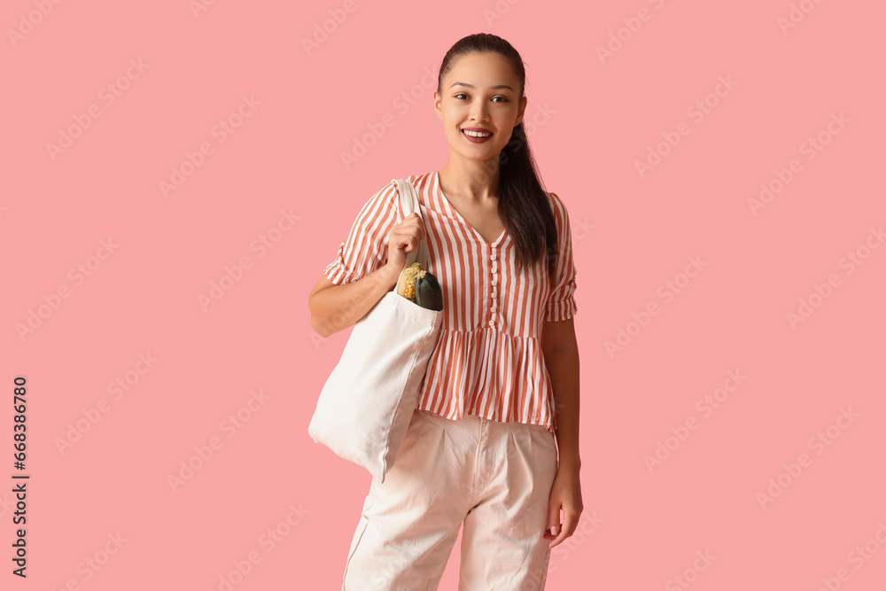 Young Asian woman with eco bag full of fresh food on pink background