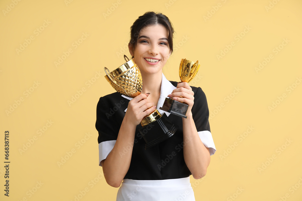 Young chambermaid with gold cups on yellow background