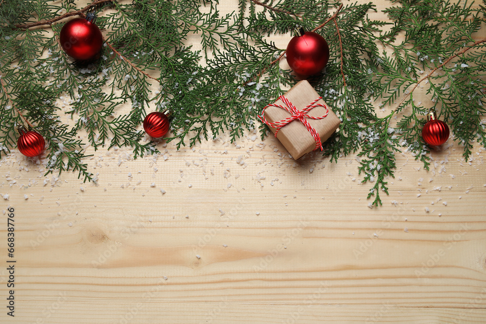 Christmas branches with gift, balls and snow on light wooden background