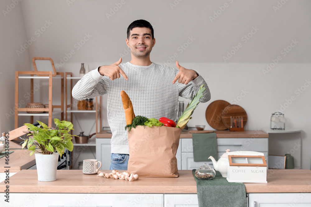 Young man pointing at grocery bag at table in kitchen