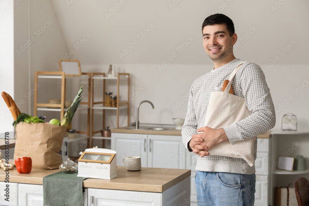 Young man with grocery bags at table in kitchen