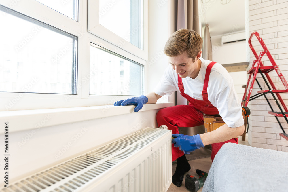 Full length shot of two professional plumbers, workers in uniform fixing or installing heating radiator. Construction, maintenance and repair concept.