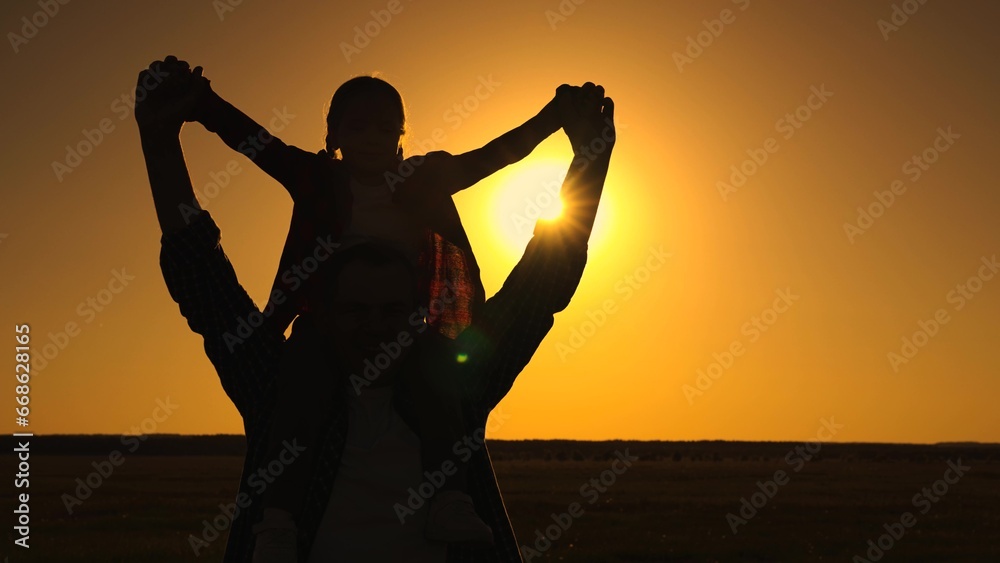 Happy family, dad, child on fathers shoulders, playing together in park against sky, mast flying, silhouette. Dad, daughter dream of flying together, family fun in outdoors. Child father walk, sunset