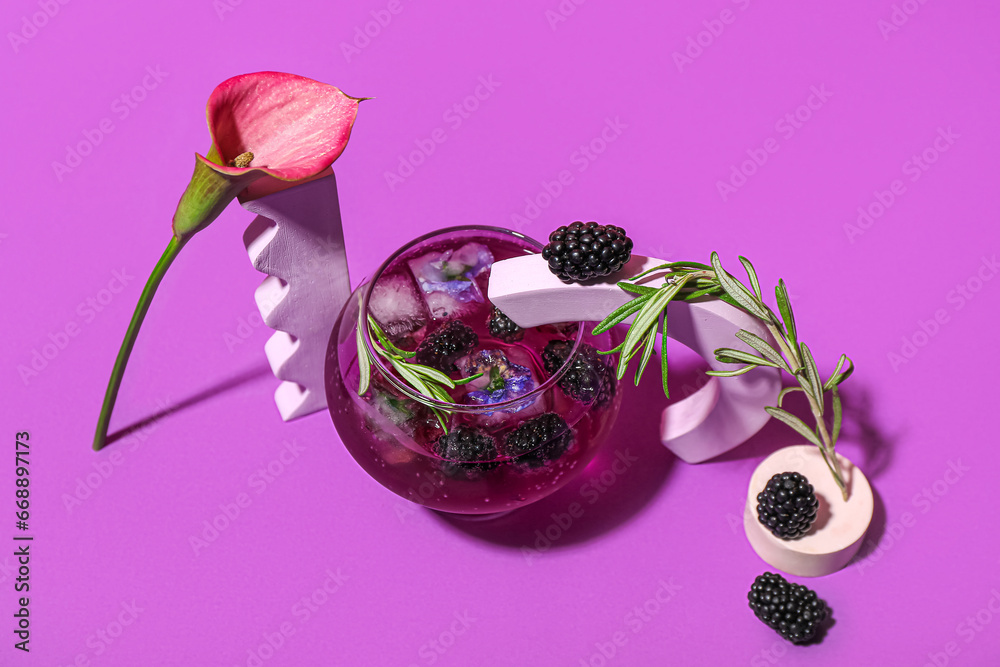 Glass of tasty blackberry cocktail with calla lily on purple background