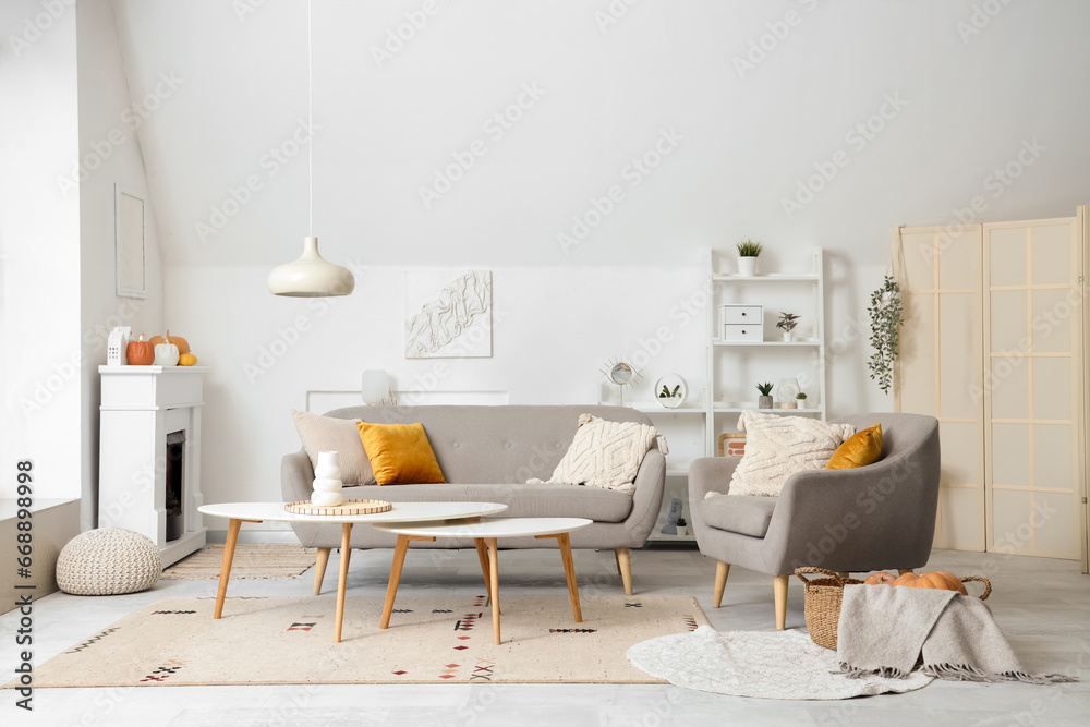 Interior of light living room with electric fireplace, armchair and sofa