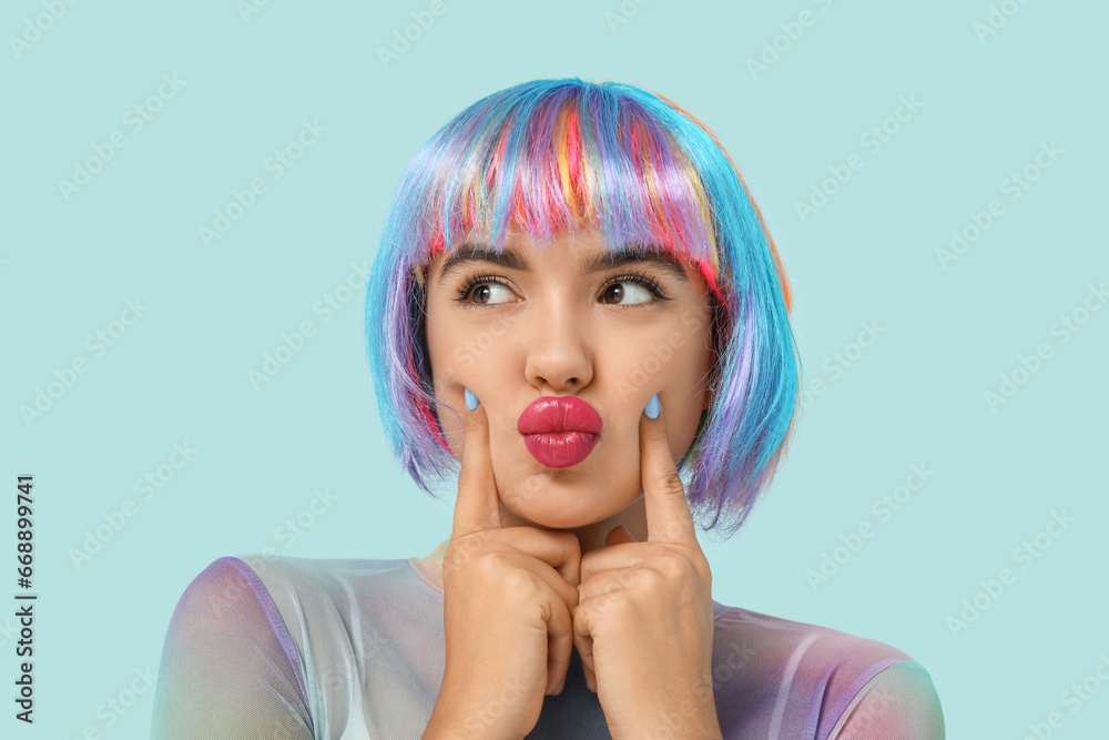 Portrait of beautiful young woman in colorful wig on blue background