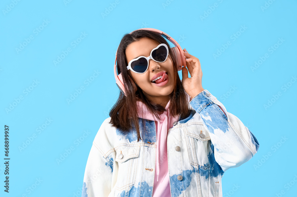 Beautiful young woman in headphones listening music on blue background