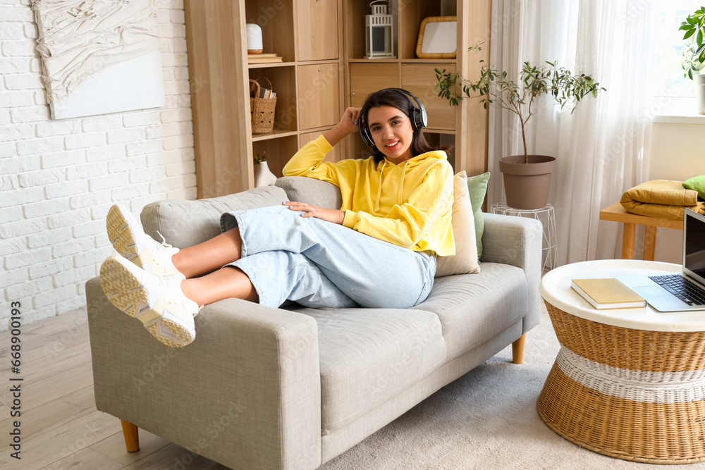 Beautiful young woman in stylish hoodie listening music at home